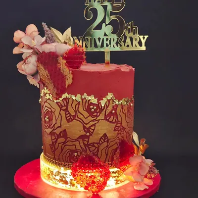 A stunning cake for a 25th anniversary, glowing with its own internal light. The design features a rich red and gold color scheme with a rose-stenciled pattern and edible, jewel-like isomalt hearts.