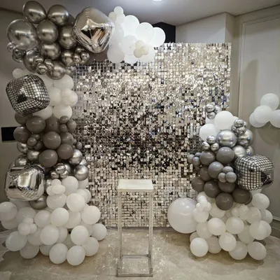 A full view of the silver shimmer wall decoration. Framed by white, grey, and silver balloons with disco ball accents, this backdrop is perfect for a glamorous party.