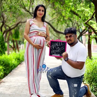 A creative announcement photo from a maternity shoot, with the father to be holding a sign that says "Miracle in Progress" while kneeling beside his partner.
