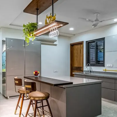 This kitchen features a large central island with an attached breakfast bar, perfect for casual meals. The design includes sleek grey cabinetry, a built-in refrigerator, and an overhead rack with integrated lighting and glass holders.