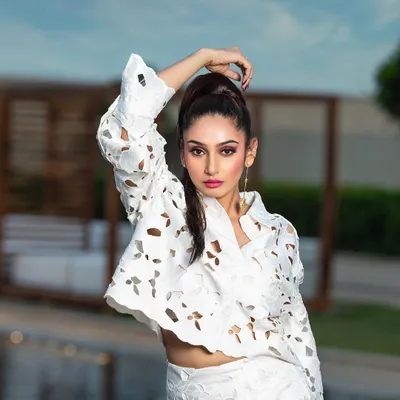 A high-fashion outdoor portrait for a magazine. The pose and high ponytail hairstyle complement the structured, modern design of the white laser-cut outfit.