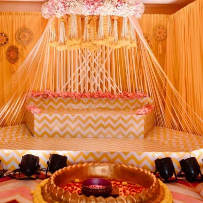 Here is the full view of the beautiful Haldi ceremony stage I designed. The setup features a canopy of hanging floral strings, a tiered seating area with a chevron pattern, and a large brass uruli in the front for the rituals.