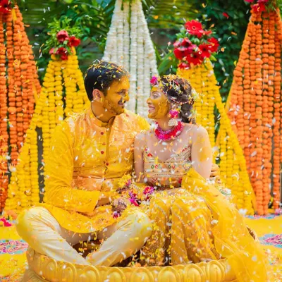 A picture-perfect Haldi moment, with the couple seated in a lotus-shaped tub, showered with flower petals against a vibrant marigold backdrop.