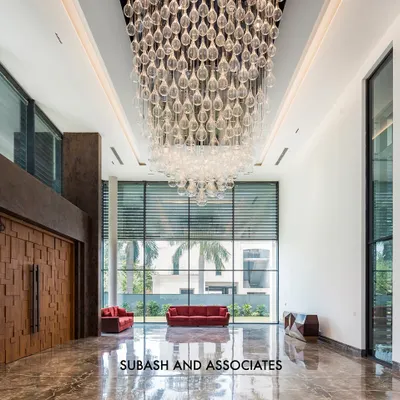 The double-height entrance lobby of a luxury residence. The grand scale is accentuated by a massive, cascading crystal chandelier, while the textured wooden door and marble floors add warmth and opulence.