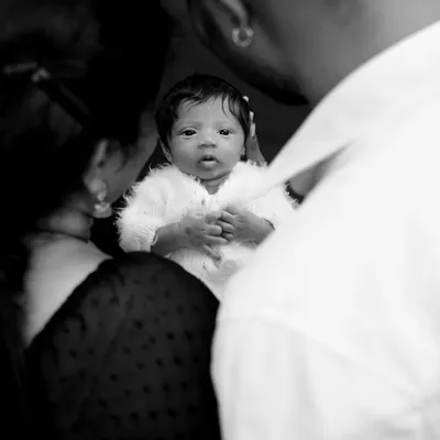 A powerful black and white portrait of a newborn looking right at the camera, held securely in their parents' arms. This image is all about connection and love.
