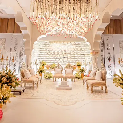 A breathtaking reception stage featuring a backdrop made of 500 crystal glasses. The stage is anchored by ornate seating and a massive floral and crystal chandelier, creating an atmosphere of pure opulence and light.