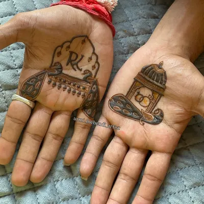 A classic groom's mehendi design. One hand features the couple's initials 'R' and 'K' inside a peacock motif, while the other has a doli (palanquin) with wedding rings, symbolizing the journey ahead.