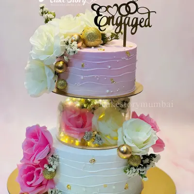An absolutely stunning floral engagement cake. This three-tier creation features a separator filled with lights and flowers, with pink and white ombre frosting and delicate gold leaf accents.