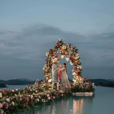 A panoramic view of the Varmala ceremony we designed on an infinity pool. The floral arch and aisle appear to float on water, creating a breathtaking backdrop against the twilight sky and the mountains of Wayanad for a truly unforgettable destination wedding.