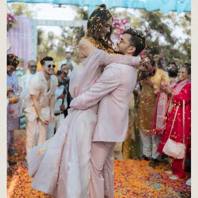 A moment of pure fun as the groom lifts the bride amidst a shower of flower petals during their Haldi carnival.