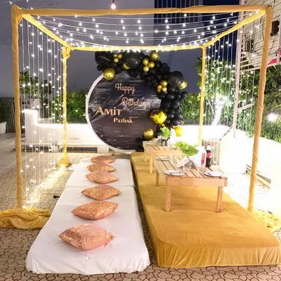 A beautiful rooftop cabana setup for a birthday. This intimate arrangement includes a canopy with fairy lights, low seating with plush cushions, and a personalized backdrop.
