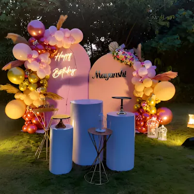 An elegant birthday party setup on a lawn for an evening celebration. This design uses two arched backdrops, a neon sign, and a sophisticated balloon arrangement in warm tones, all beautifully lit.
