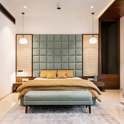 This serene bedroom features a large, sage green tufted headboard that creates a soft and inviting focal point. Pendant lights hang on either side of the bed, providing warm, ambient light perfect for unwinding.