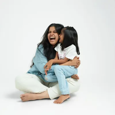A mother and daughter sharing a moment of pure, uninhibited laughter. The simple white background of the studio puts their joyful connection at the center of the portrait.