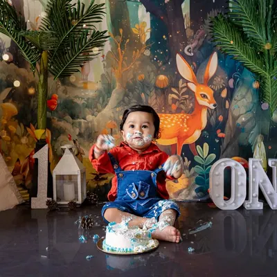 A wide-angle view of the woodland-themed first birthday cake smash, showing the full setup with a teepee tent and forest backdrop. The baby is having a wonderful time exploring the cake.
