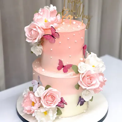 This two-tiered 50th birthday cake is adorned with an arrangement of handmade pink sugar flowers and delicate butterflies, creating a soft and celebratory design.