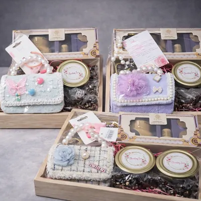 A beautiful collection of birthday hampers for a baby girl. Each wooden tray is filled with an aroma diffuser, chocolates, cookies, and a cute mini handbag, available in different pastel colors.