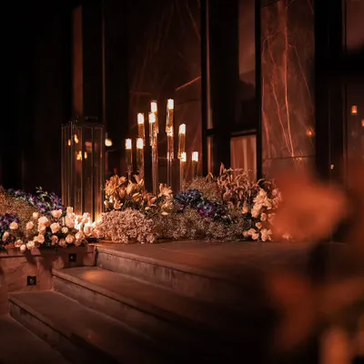 We used tiered floral arrangements and dozens of candles of varying heights to create a dramatic and romantic pathway. This design element guided guests through the space while adding depth and a warm, inviting glow to the evening decor.