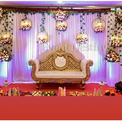 An elegant stage setup for an engagement or reception. The design features a white drape backdrop with hanging floral hoops and uplighting for a magical effect.