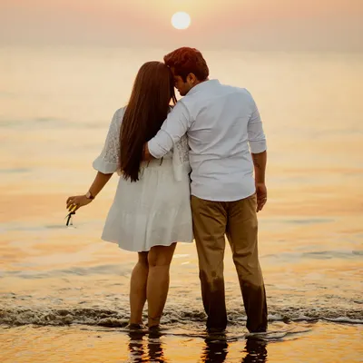 A classic romantic silhouette against a breathtaking sunset. The couple stands at the water's edge, watching the sun dip below the horizon, creating a timeless and serene pre-wedding portrait.