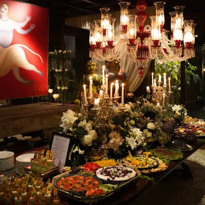 An opulent grazing table set for a grand celebration, featuring a lavish spread of international cheeses, fresh fruits, artisanal breads, and gourmet appetizers. The setup is accented with dramatic candelabras and floral arrangements, creating a truly luxurious focal point.
