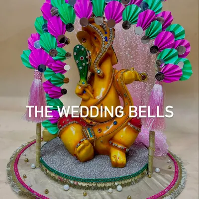 Welcome Bappa home with a custom mandap from us. This vibrant design features a Ganesha idol placed on a decorative platform, framed by a colorful arch made of pink and green paper fans with mirror work.