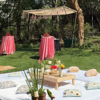A wide view of our luxury picnic setup. We arranged low tables with cushions on soft white rugs, with standing cocktail tables covered in pink linens under a canopy for a varied and functional layout.