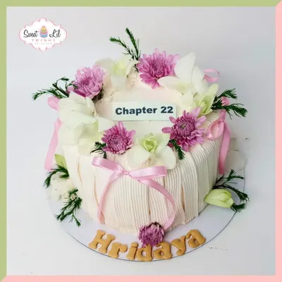This elegant "Chapter 22" cake is a beautiful way to mark a new year. The design features a delicate pleated frosting effect, soft pink ribbons, and a crown of fresh, beautiful flowers like orchids and chrysanthemums.
