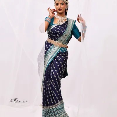 A full-length professional shot showcasing a complete look. The navy blue and teal saree is draped to perfection, complemented by traditional jewelry and a confident pose.