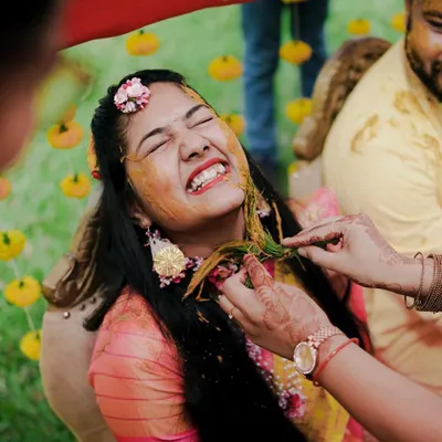 The pure, unadulterated joy of a Haldi ceremony! This close-up captures the bride's ecstatic laugh as she gets playfully smeared with turmeric paste.