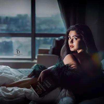 A moody and intimate portrait of actress Ritabhari Chakraborty. The soft light from the window and the cozy bedroom setting create a contemplative and personal atmosphere.