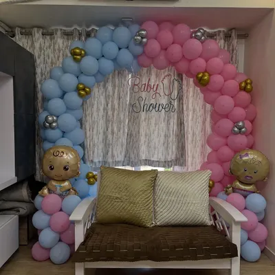 A classic "boy or girl" baby shower theme with a balloon arch split between blue and pink. The setup includes a comfortable chair for the mom-to-be and cute baby foil balloons.