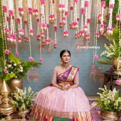 The bride, looking serene and beautiful, seated for her pre-wedding rituals. I created a stunning backdrop with hanging garlands of jasmine, lotus buds, and pink carnations, set against a custom-painted traditional mural.