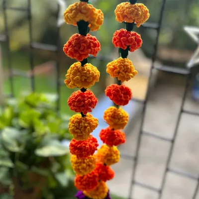 A close-up of my crochet marigold garland hanging by a window. The alternating yellow and orange flowers look just as fresh and vibrant as real genda phool, bringing cheer to any space.