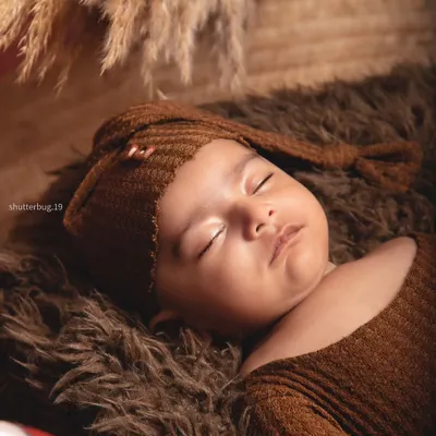 A close-up of a sleeping three-month-old boy, looking so peaceful in his cozy brown outfit and hat.