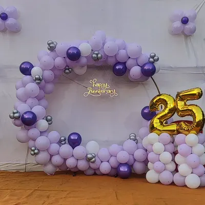 A large circular balloon backdrop designed for a 25th anniversary celebration. This photo-ready installation uses a lavender, purple, and silver color scheme with a "Happy Anniversary" neon sign.