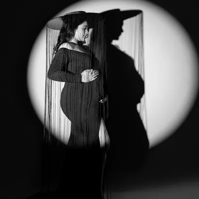A dramatic black and white portrait using shadow and light. The spotlight creates a powerful silhouette, while the fringed hat adds a touch of vintage mystery and style.