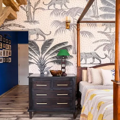 This master bedroom is a room of surprising contrasts. A cantilevered staircase and a bold cobalt blue wall lead into the main space, where a towering 16-foot ceiling is grounded by a four-poster bed. The jungle-themed wallpaper adds a touch of wildness, creating a dramatic yet deeply personal retreat.
