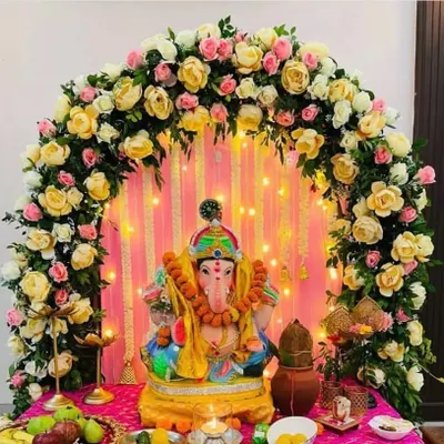 I design classic and elegant Ganpati backdrops. This beautiful setup features an arch of yellow and pink roses over the idol, with a backdrop of delicate string lights that create a warm, divine glow.
