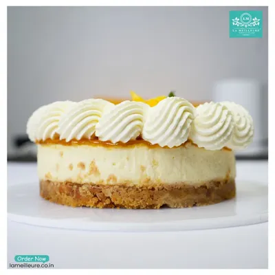 A side view of our creamy Mango Cheesecake. You can see the thick, buttery biscuit base, the rich cream cheese layer, and the fresh mango topping with piped cream.