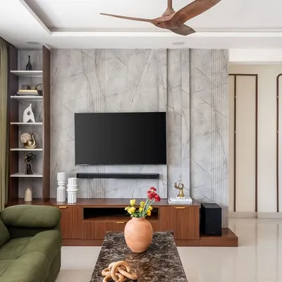 This living room in 'The Flux Abode' project features a textured grey media wall and rich walnut cabinetry. The design combines contemporary sophistication with warm, natural materials for a balanced and inviting feel.