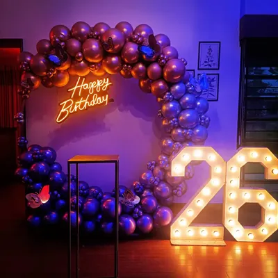 A complete birthday setup for a 26th celebration, featuring a full balloon ring in chrome purple and rose gold. The decor is enhanced with a custom 'Happy Birthday' neon sign and large, illuminated marquee numbers.