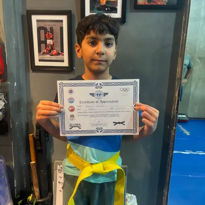 The first of many victories. This young student is proud to receive his yellow belt and certificate after passing his Level One kickboxing test.