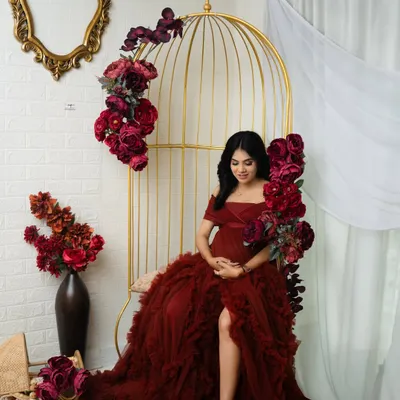A moment of quiet contemplation in our floral paradise setup. The rich red gown and matching flowers create a stunning, monochromatic look against the golden birdcage chair.