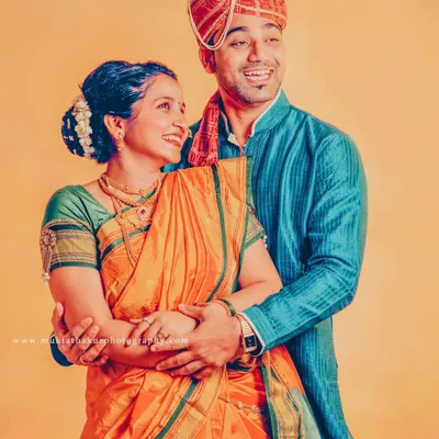 A classic portrait of a Maharashtrian couple. Her vibrant Paithani saree and his traditional kurta and pagdi look beautiful against the warm, solid background.