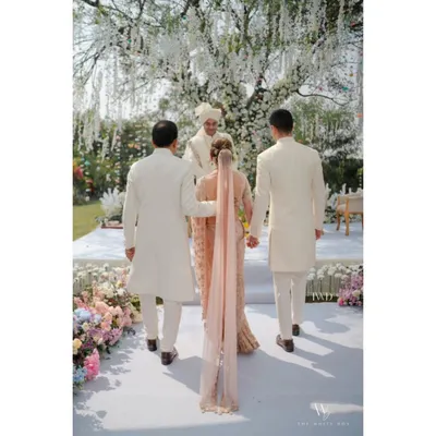 A beautiful moment as the bride walks towards her happily ever after, escorted down a pristine white aisle lined with lush pastel florals. This is the essence of a dreamy garden wedding.