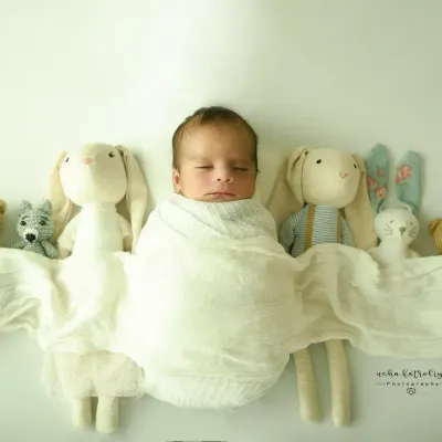 A sweet lineup of stuffed animal friends. This minimalist portrait on a clean white background keeps the focus entirely on the baby, surrounded by their soft toys.