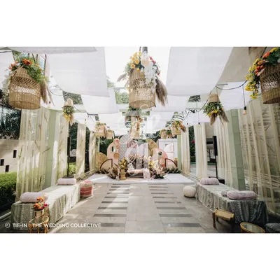 A wide view of our boho-pastel Mehendi setup, designed for a relaxed sundowner celebration. The space features low lounge seating, printed drapes, and hanging baskets filled with flowers, creating a comfortable and chic atmosphere.