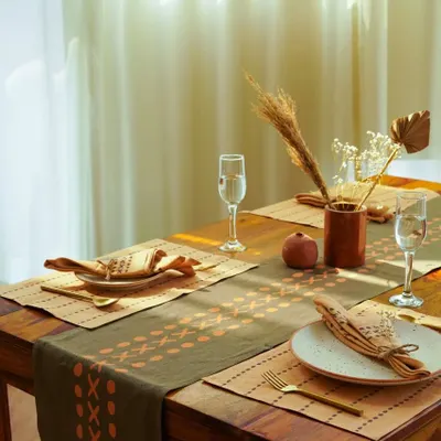 A beautifully set dining table featuring block-printed mats and napkins. The warm, natural light and earthy tones create a homely and inviting atmosphere for this tableware brand.