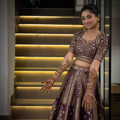 A beautiful, smiling bride in her full wedding attire, proudly showing the intricate mehandi we designed to complete her look.